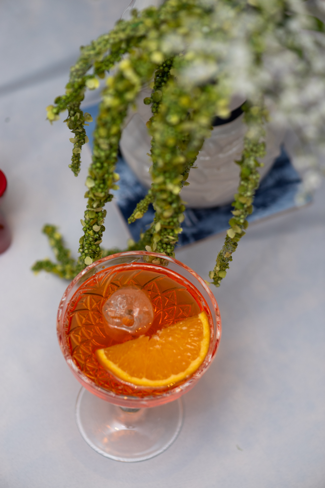 A vibrant orange cocktail with an orange slice served on a blue patterned tile coaster at Dutch Masters Studio