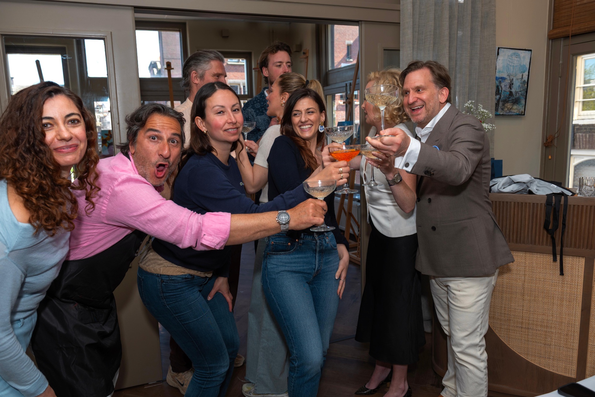 Lively group of guests raising coupes and cocktail glasses together at Dutch Masters Studio